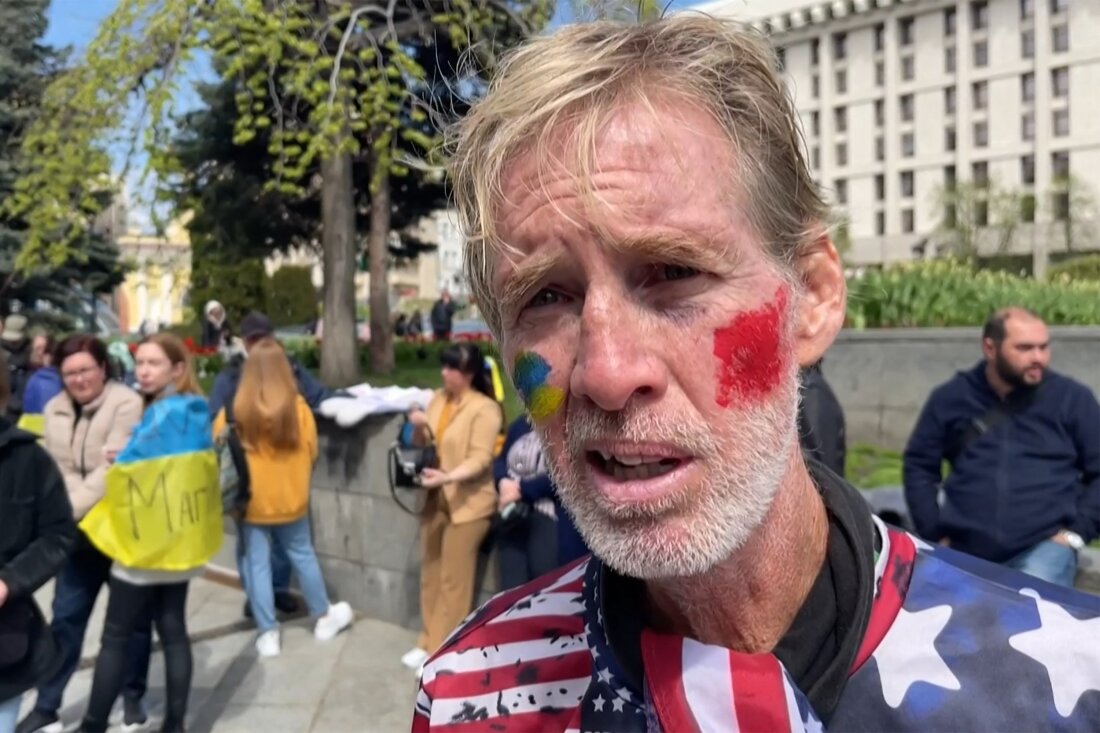 A screenshot shows a man at a rally, with his cheeks painted red and yellow and blue in support of Ukraine.