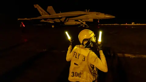 Getty Images A flight deck crew member signals as an F/A-18 Super Hornet fighter jet takes off from the flight deck of the USS Dwight D. Eisenhower (CVN 69) aircraft carrier during operations in the southern Red Sea